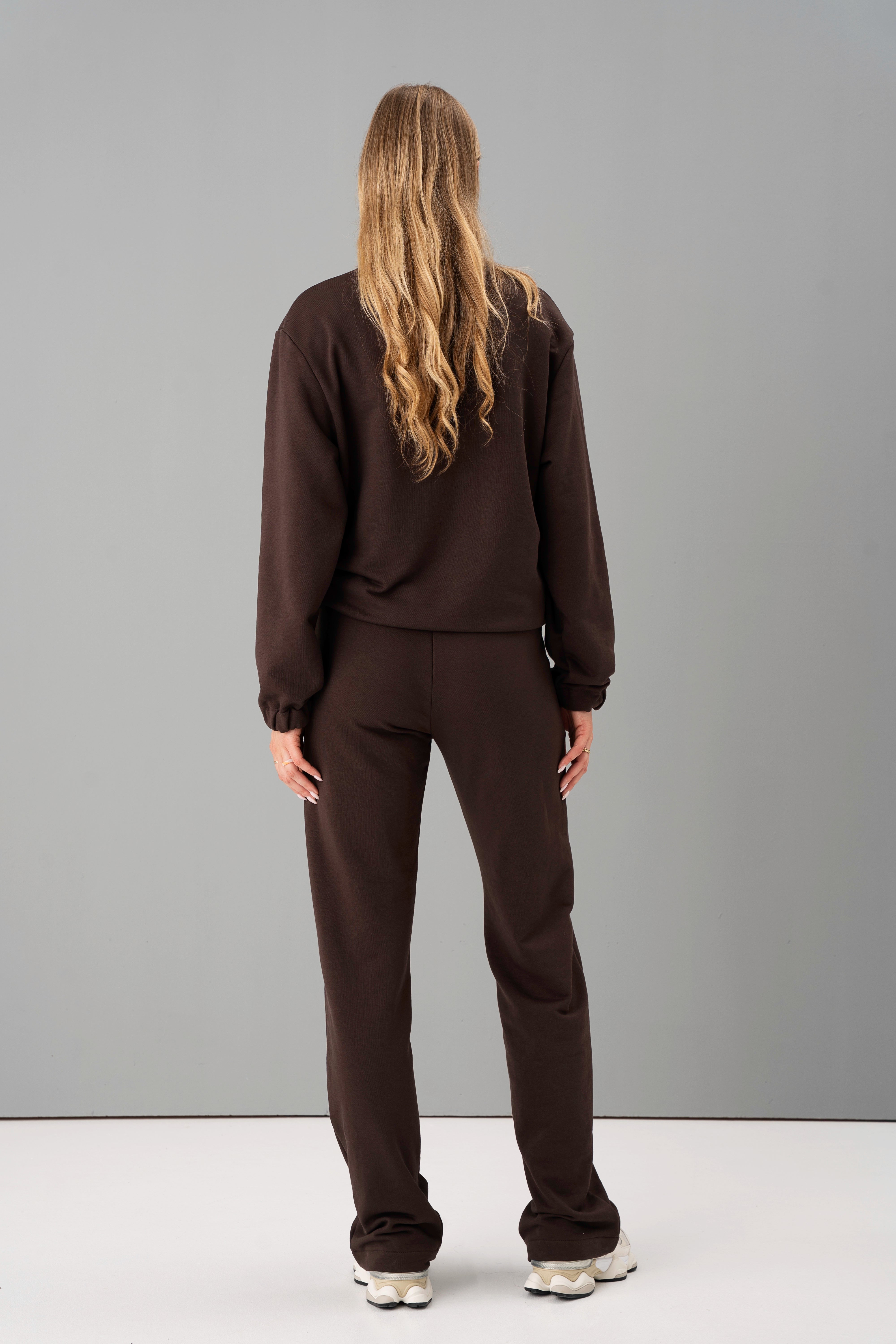 modelis su tamsiai rudos spalvos treningais mėja, stovinti iš nugaros, ilgi plaukai laisvai krenta