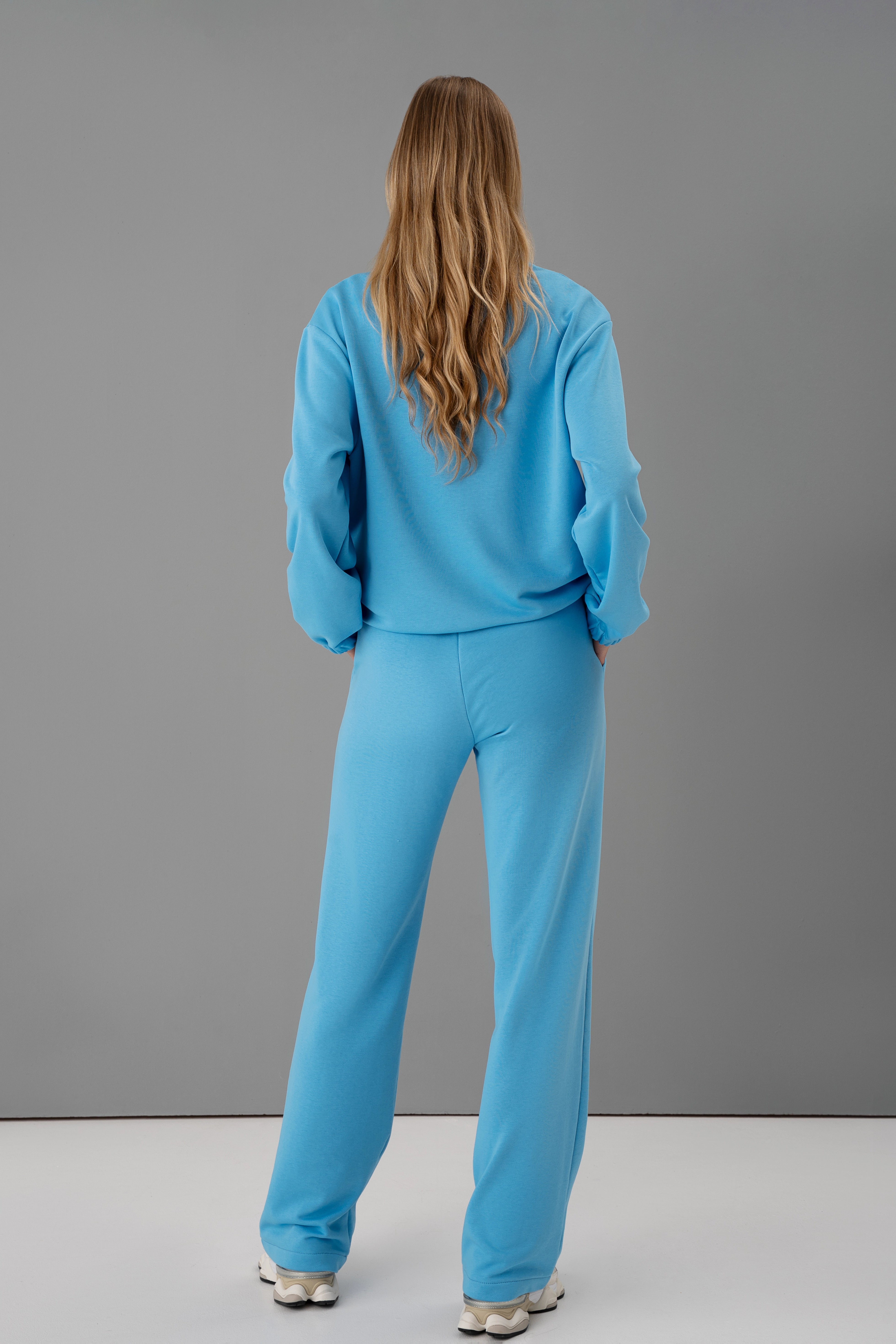 moteris vilki cutmyfashion mėlynos spalvos kostiumą, atsukusi nugarą kamerai, studijos fonas