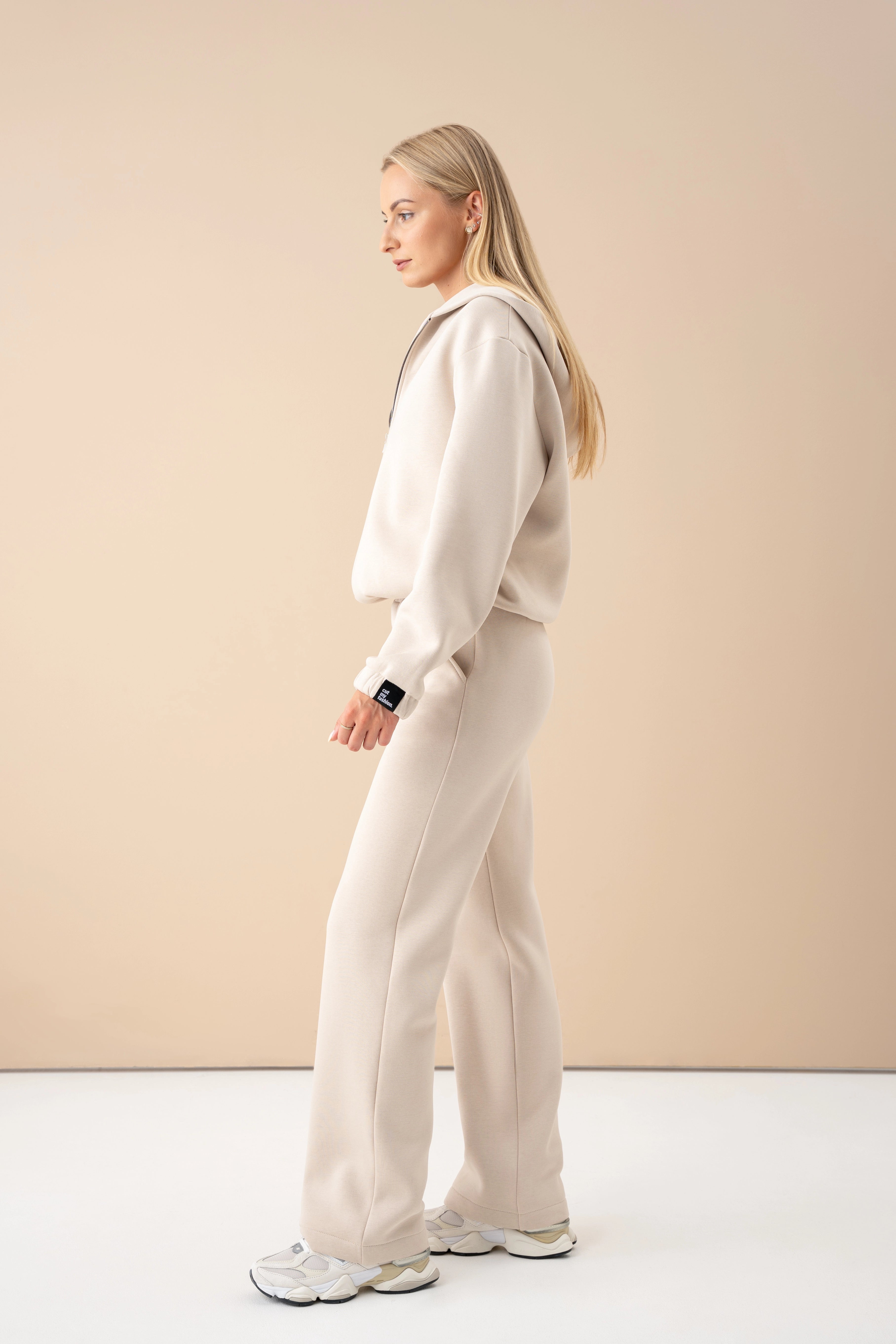 moteris dėvi oversized džemperį ir kelnes, eina studijos aplinkoje, vaizdas iš šono