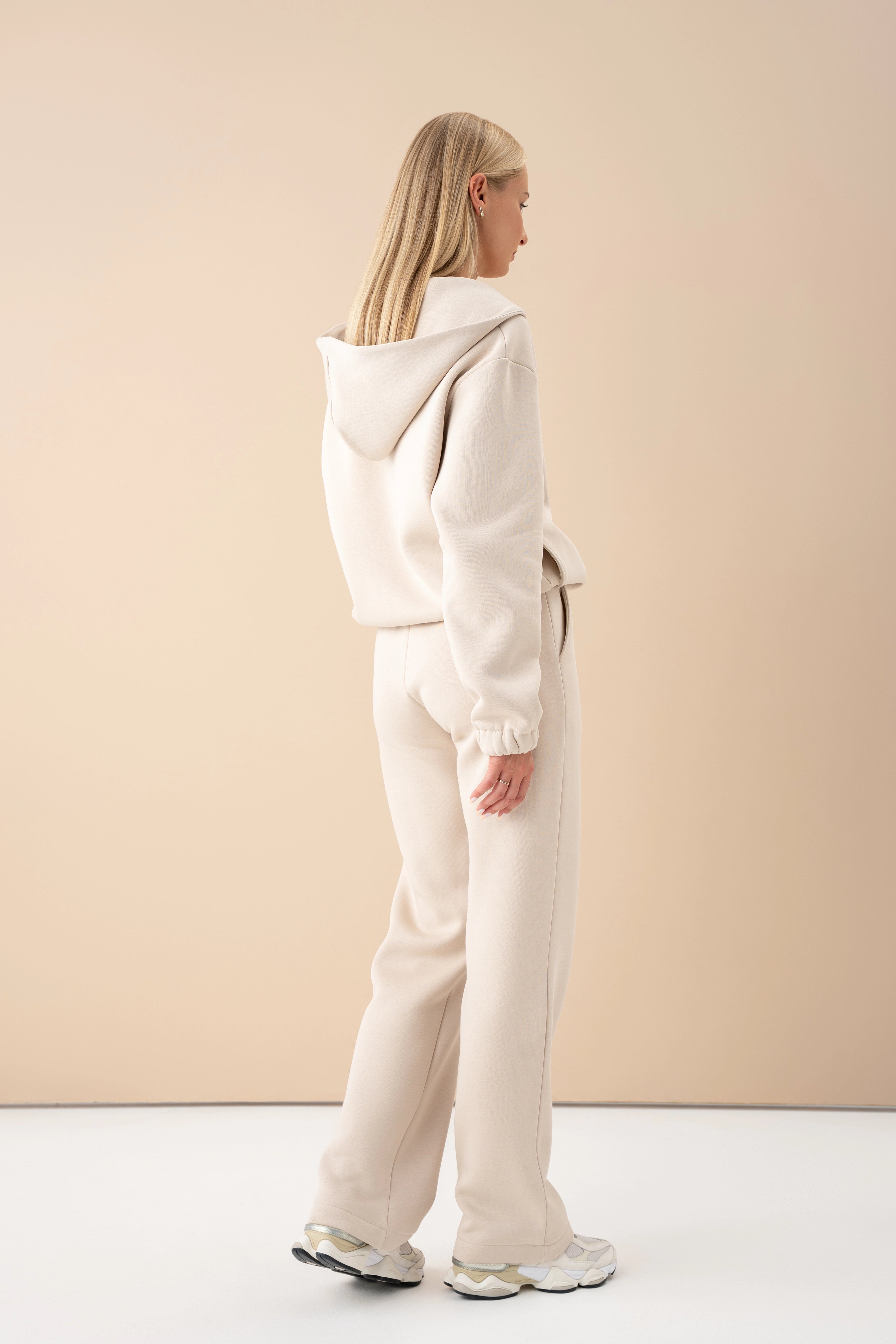 modelis su šviesiais treningais atsukta nugara, demonstruoja gobtuvą, fone šviesi siena