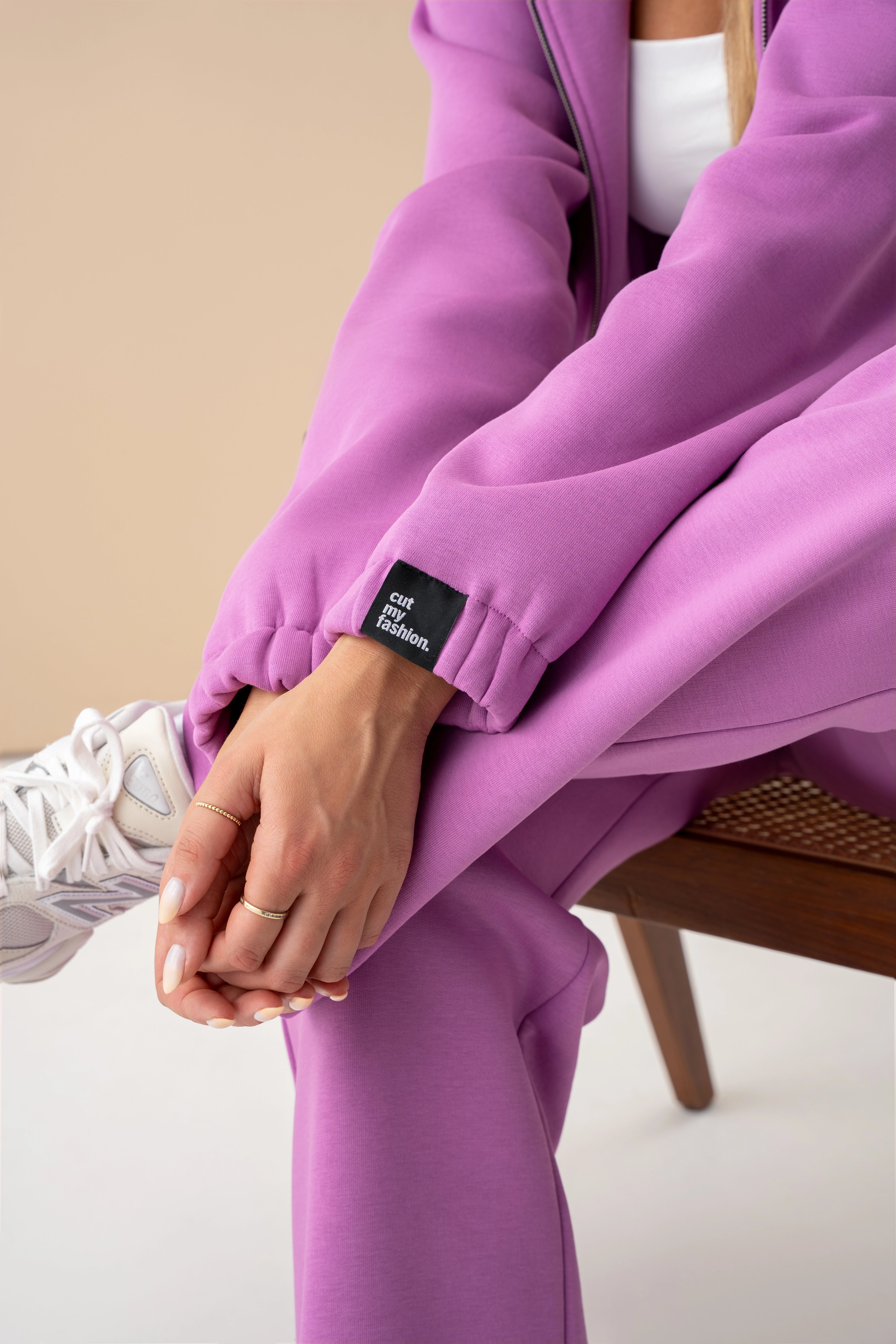 artimas kadras su pastelinės rožinės spalvos cutmyfashion rankove ir baltais sportiniais bateliais, modelis sėdi ant kėdės