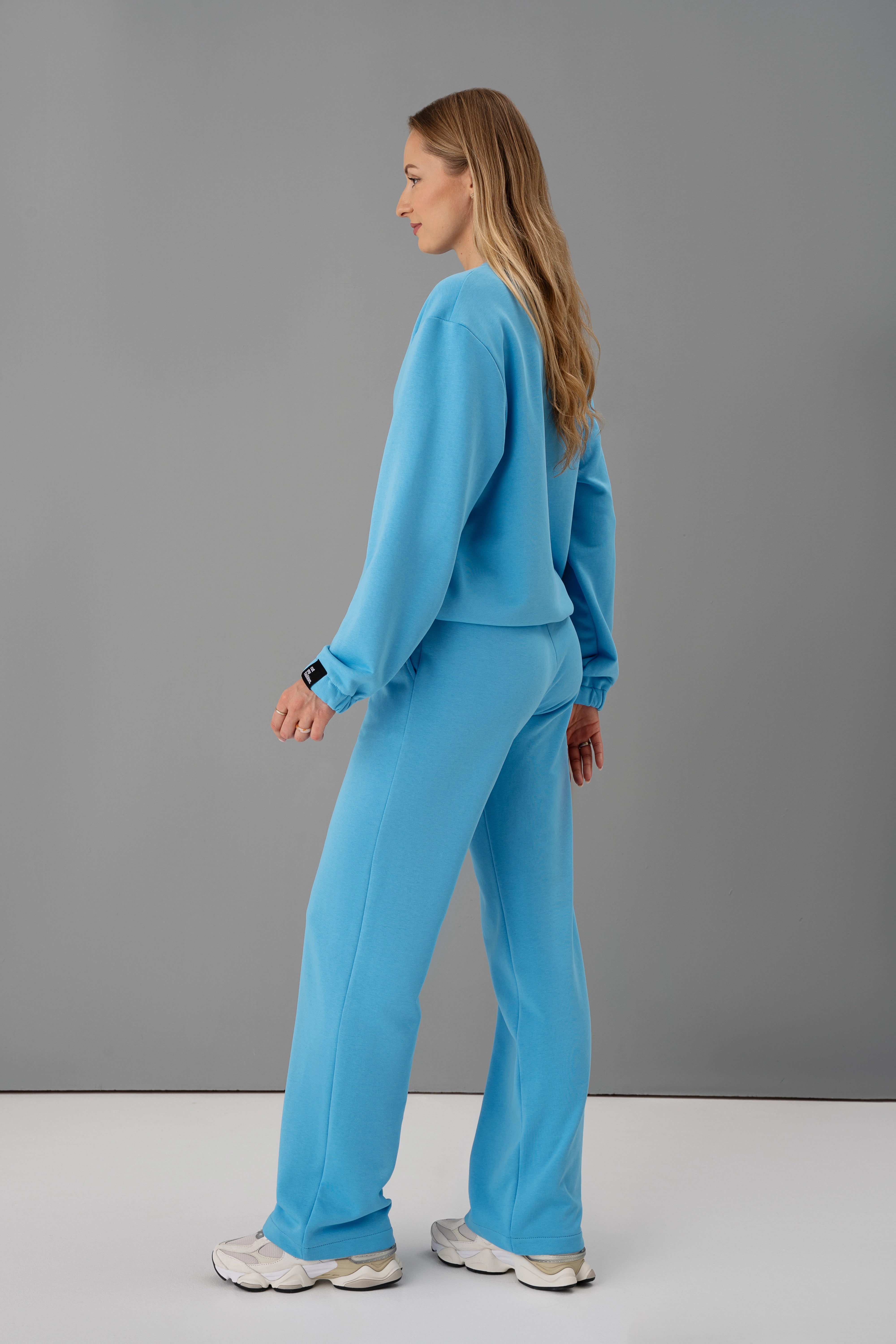 modelis dėvi mėlyną cutmyfashion kostiumą be pūkelio, pozuoja studijoje nusisukusi šonu