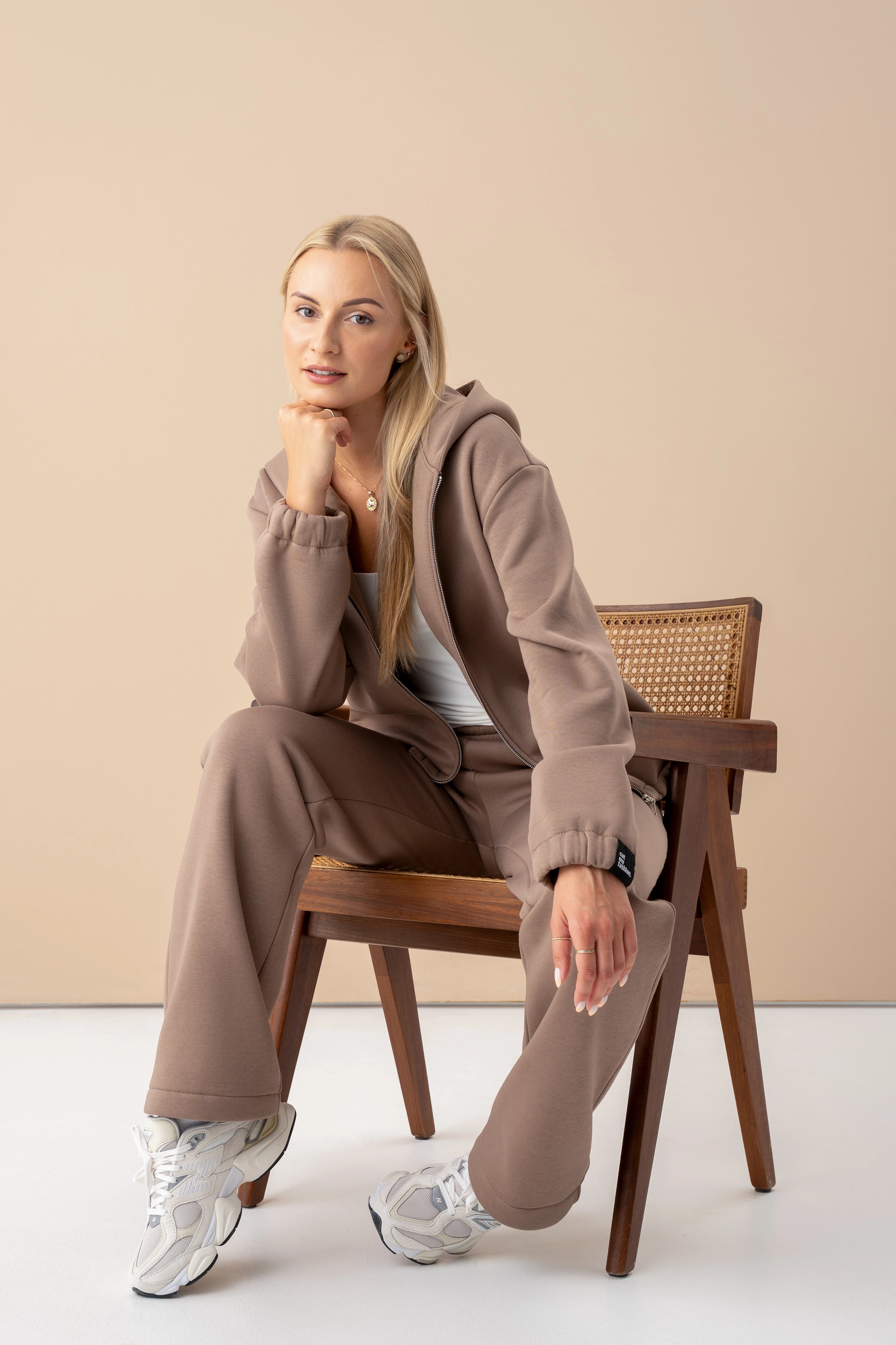 moteris su latte spalvos cutmyfashion treningų komplektu sėdi ant medinės kėdės, žiūri į objektyvą, pagaminta Lietuvoje