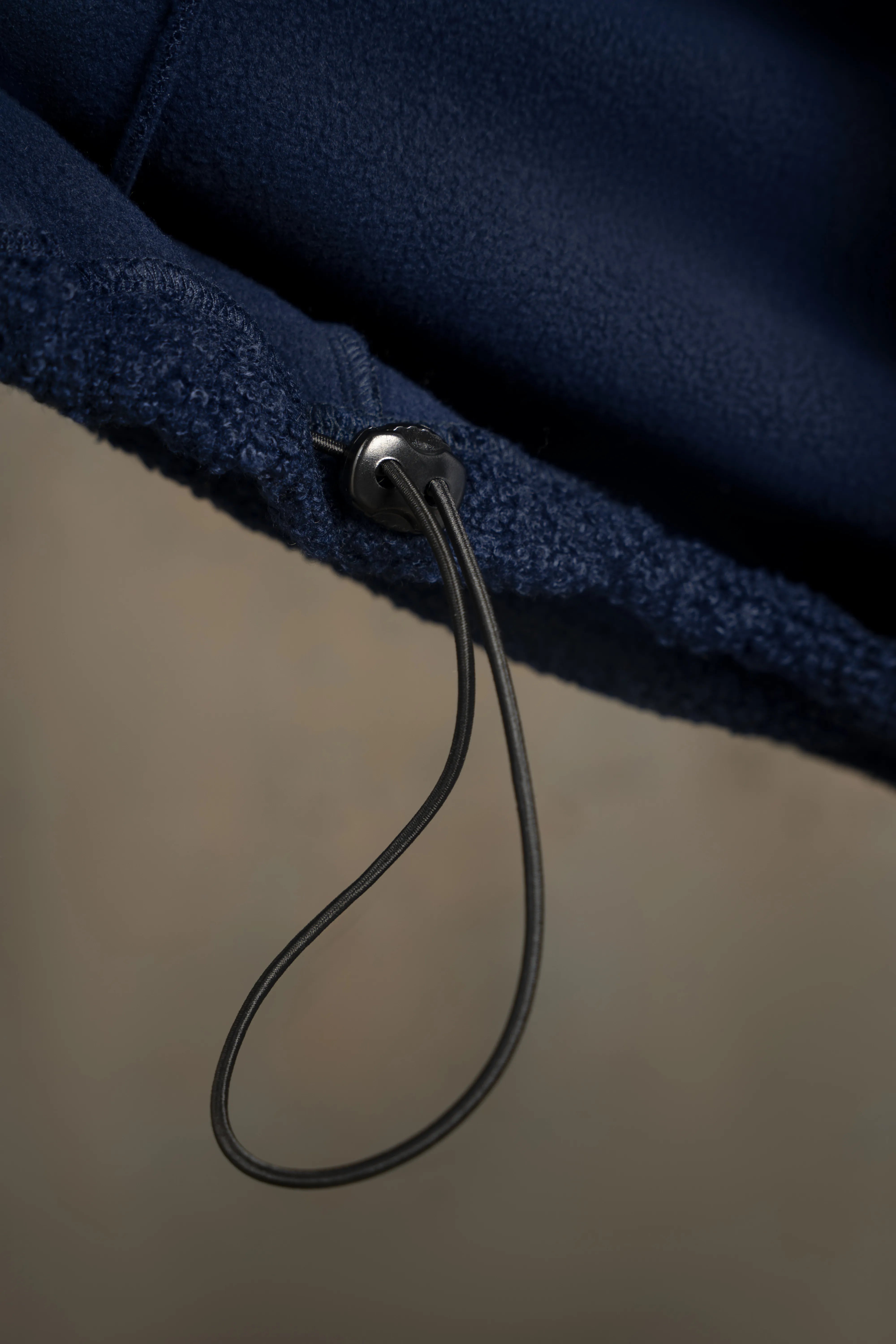 Tamsiai mėlynos spalvos vyriško džemperio apačios reguliavimo virvelės ir siūlės detalė